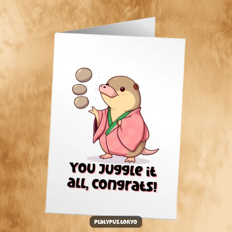 Funny Free Printable Congratulations Card: a platypus in a vibrant kimono playfully juggles three smooth, round pebbles, celebrating skill.
